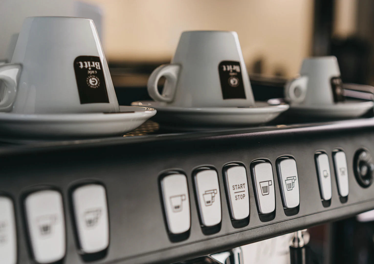 Gray coffee cups on a coffee machine with control buttons in the foreground.