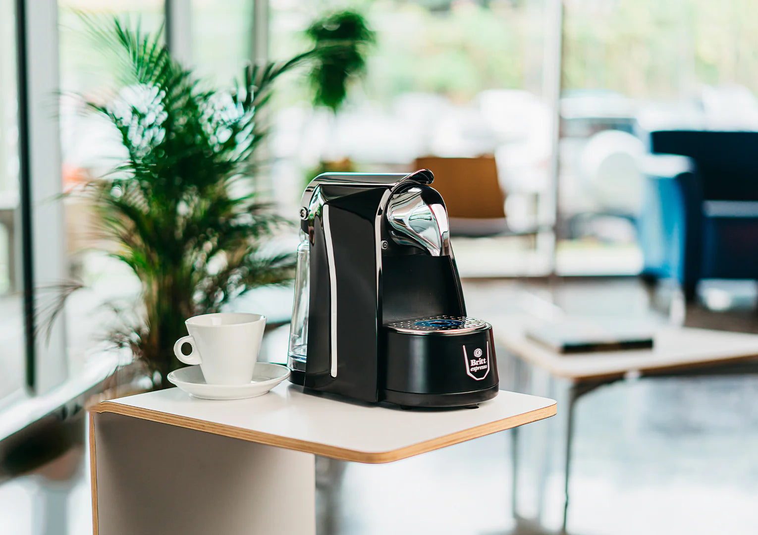 Black coffee machine on a small table with a cup of coffee in a bright room.