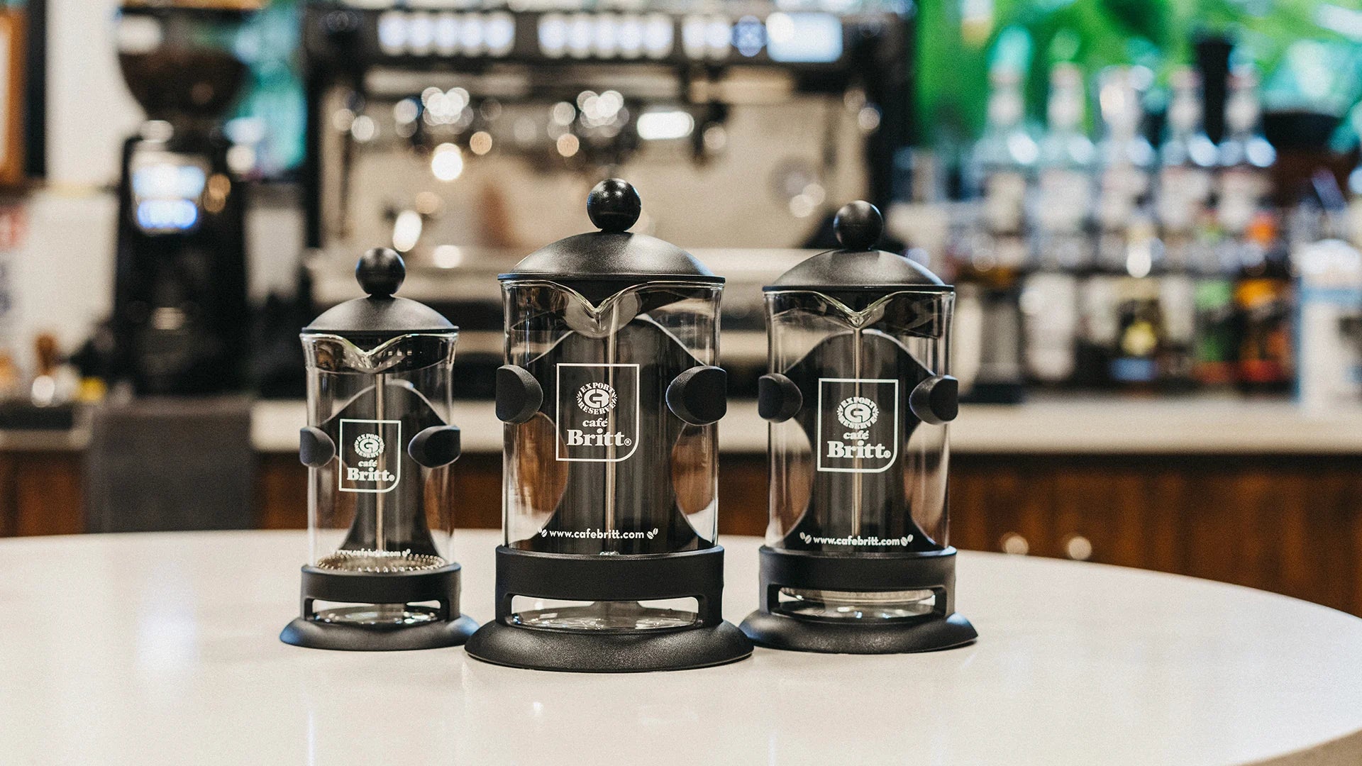 Three french press coffee makers on a counter with a blurred background.
