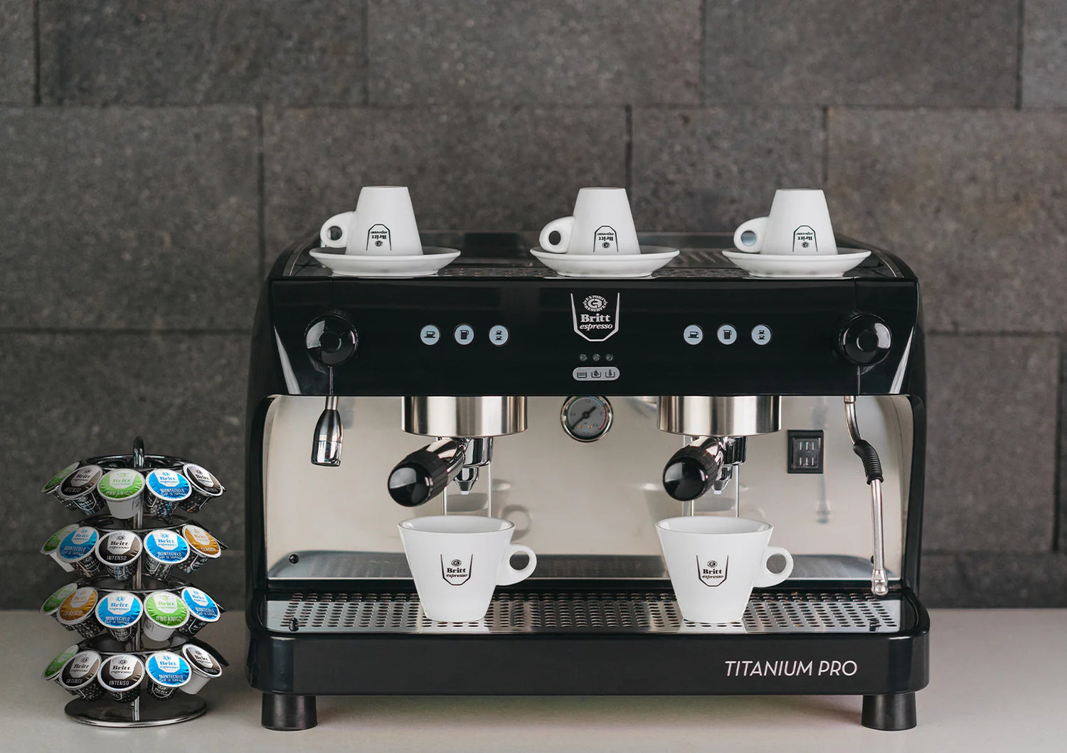 Espresso machine labeled 'Titanium Pro' with coffee cups and a pod holder on a gray stone background