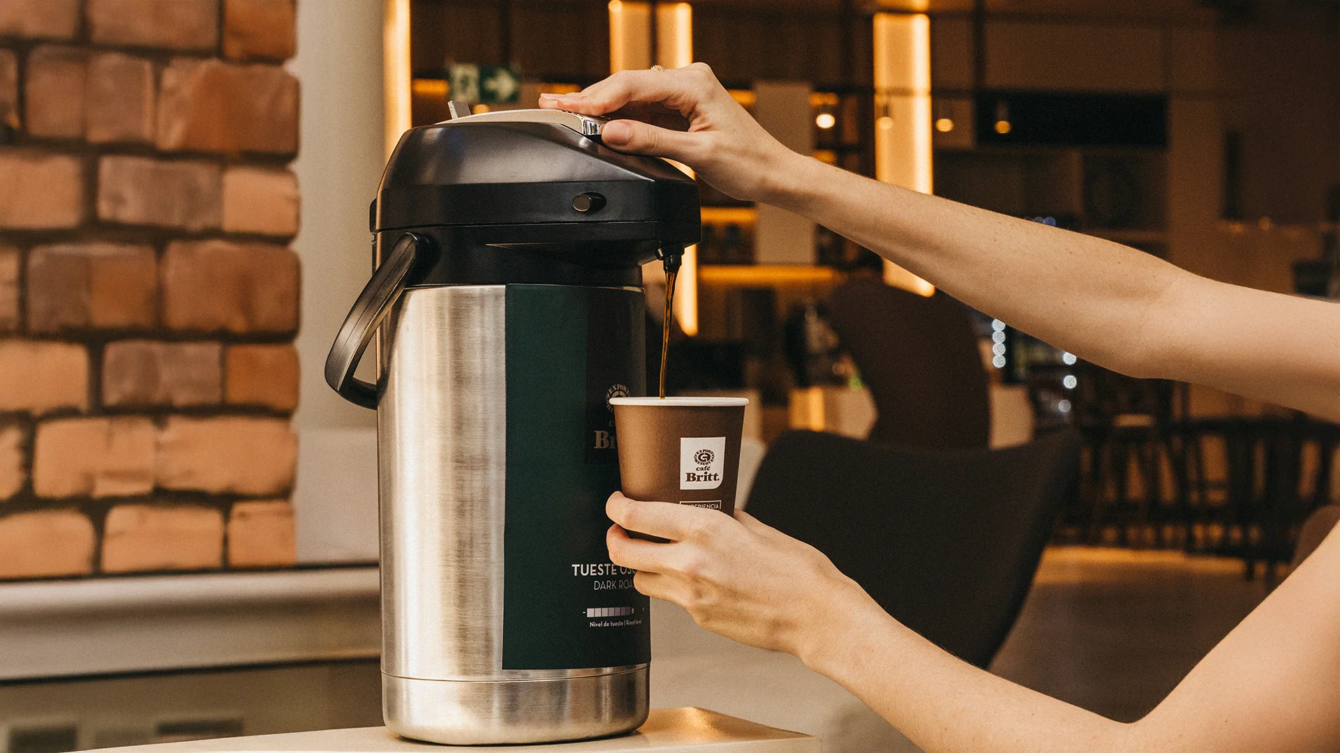 Person pouring coffee from a thermos into a cup in a cozy indoor setting.