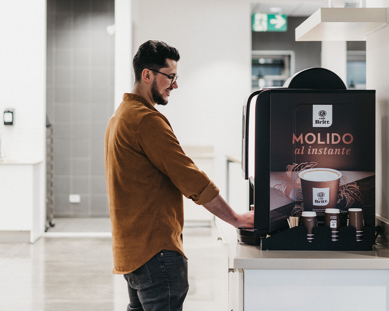 Employee using a Café Britt commercial coffee machine in a modern office break room.