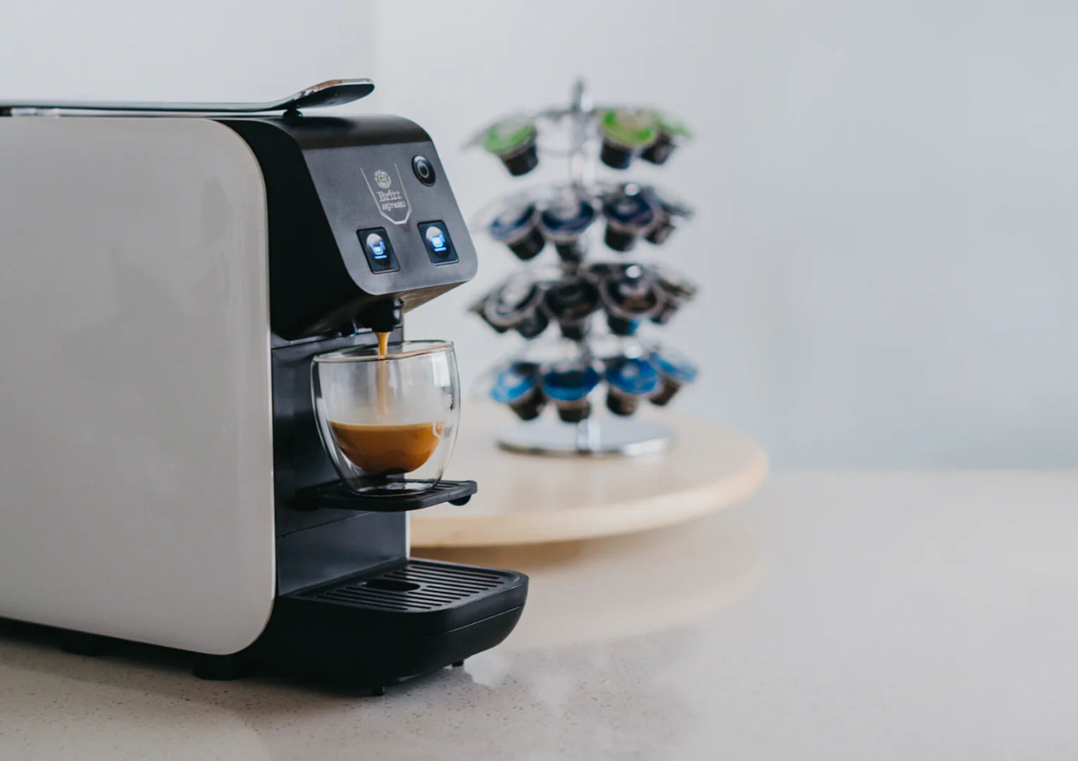 Kubo Britt Espresso machine dispensing coffee into a glass on a light surface with a blurred background