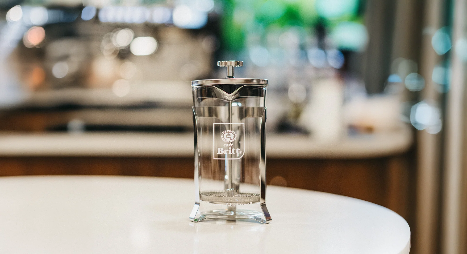 Clear glass coffee press with brand logo on a blurred kitchen counter