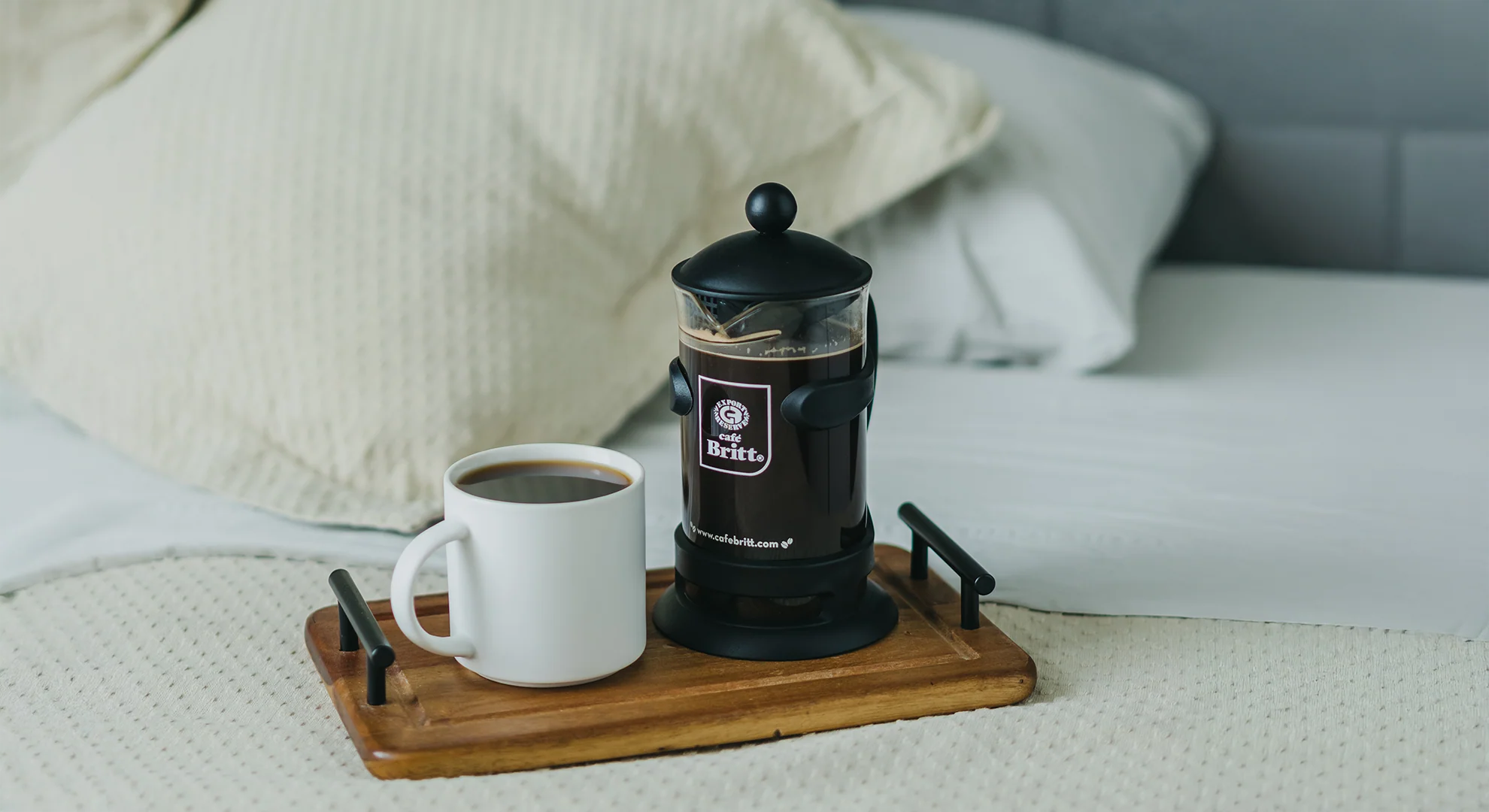 Black Britt coffee press and white mug on a wooden tray with pillows in the background
