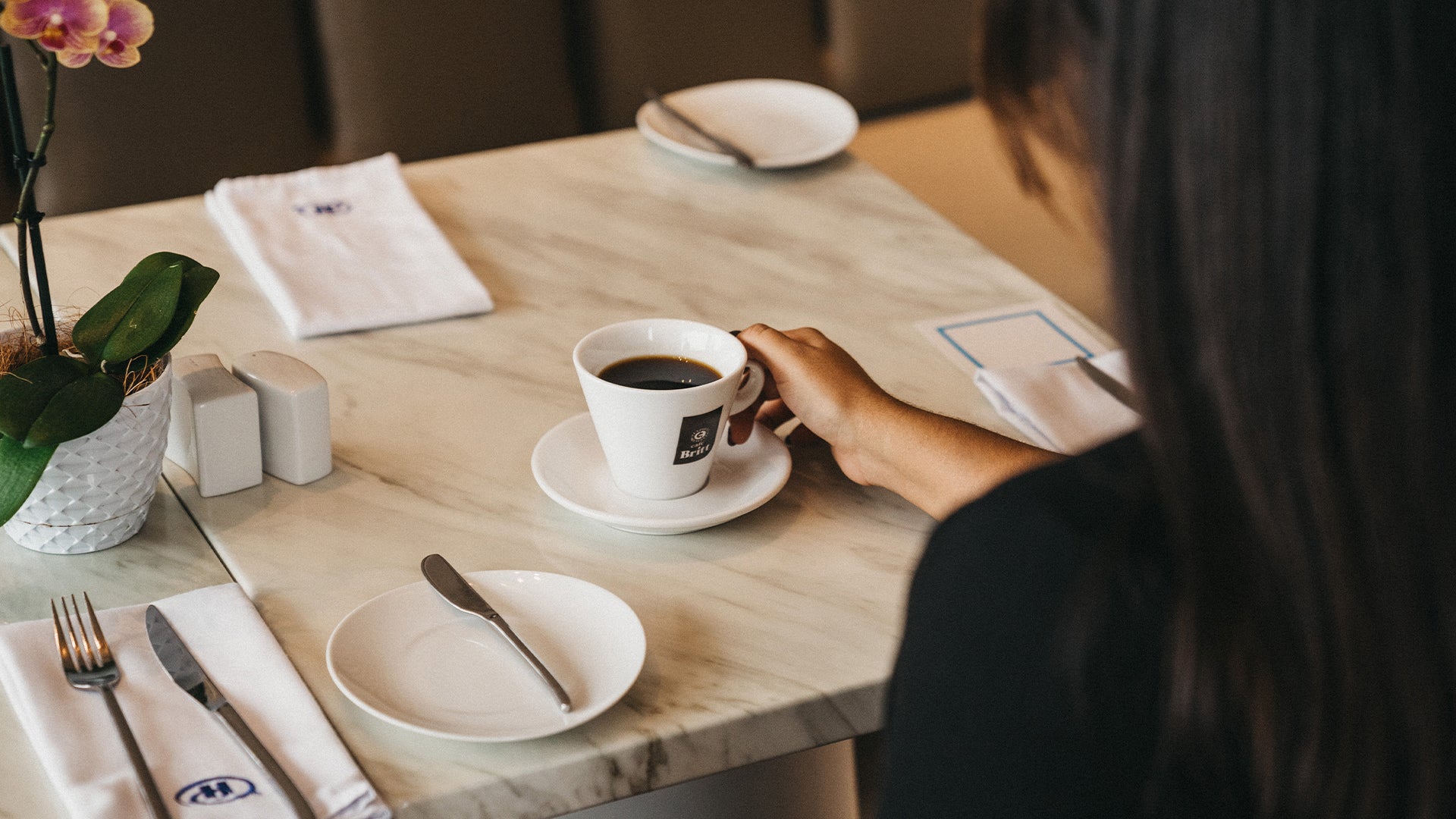 Person holding a cup of Café Britt gourmet Costa Rican coffee at a restaurant table.