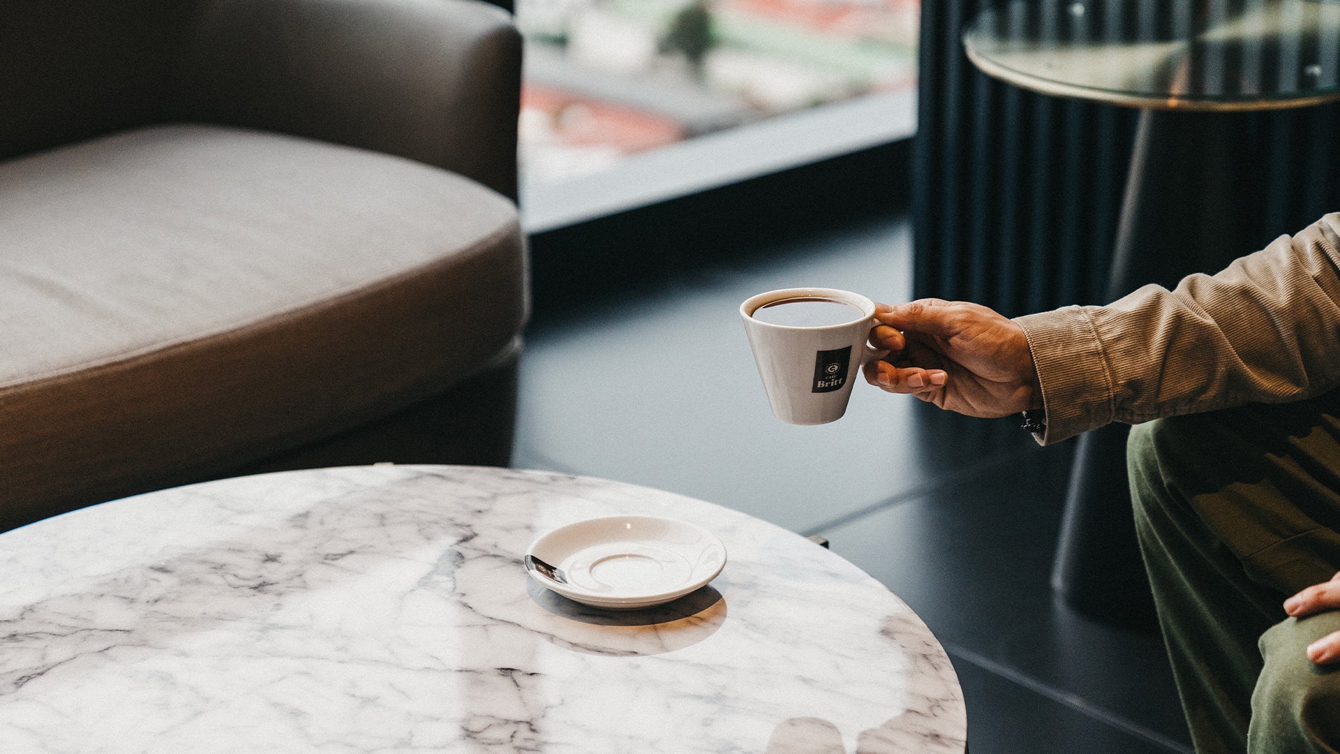 Person holding a Café Britt coffee cup in a modern office lounge, showcasing premium coffee solutions for businesses.